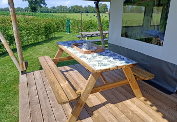 Træbord og bænk på terrasse ved safaritelte på Farm Campsite de Katreel i Holland, solrig dag.