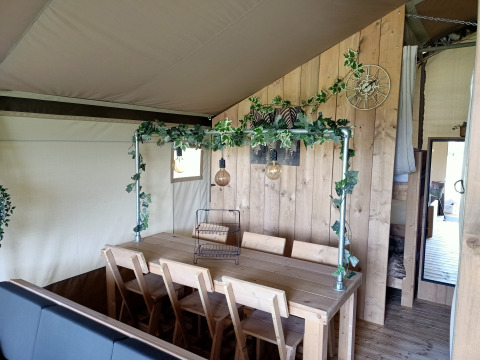 Interior de tienda safari en Farm Campsite the Katreel con mesa de madera y decoración verde natural.
