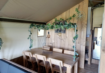 Indretning af safari-telt på Farm Campsite the Katreel med træbord, stole og grønne dekorationer.