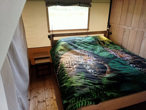Interno di una tenda safari al Boerderijcamping het Katreel, Paesi Bassi, con letto e copriletto leopardo.