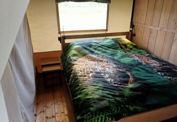 Interior de una tienda safari en Boerderijcamping het Katreel, Países Bajos, con cama y ropa de leopardo.