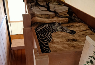 Safari-Zelt mit gemütlichem Holzbett und Zebradecke auf dem Bauernhofcampingplatz het Katreel in den Niederlanden.