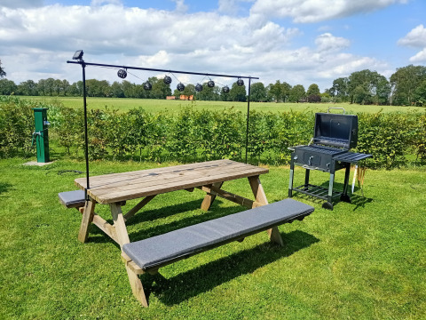 Outdoor picnic table and grill on green grass under a blue sky at Farm Campsite the Katreel, Netherlands.