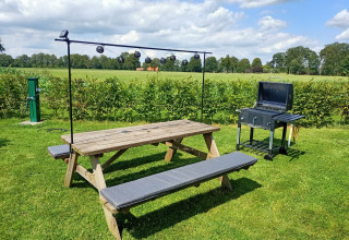 Outdoor picnic table and grill on green grass under a blue sky at Farm Campsite the Katreel, Netherlands.