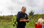 Mand viser børn planter på FarmCamps De Kamperhoek, en feriepark i Zeeland, Holland, under overskyet himmel.