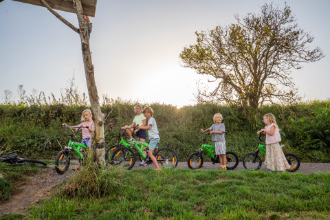 Kinder spielen mit grünen Fahrrädern im Freien bei FarmCamps De Kamperhoek in Zeeland, Niederlande.