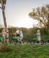 Niños juegan al aire libre con bicicletas verdes en FarmCamps De Kamperhoek, parque de vacaciones en Zeeland.