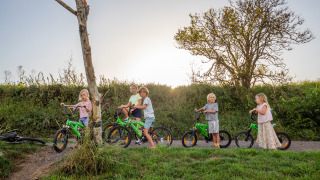 Niños juegan al aire libre con bicicletas verdes en FarmCamps De Kamperhoek, parque de vacaciones en Zeeland.
