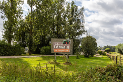 Welkomstbord bij FarmCamps De Kamperhoek vakantiepark in Zeeland, Nederland, omgeven door groen en bomen.
