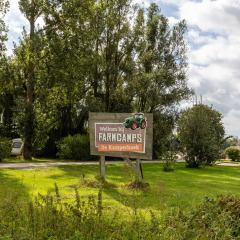 Cartel de bienvenida en FarmCamps De Kamperhoek, un parque vacacional en Zelanda, Países Bajos, rodeado de verde.
