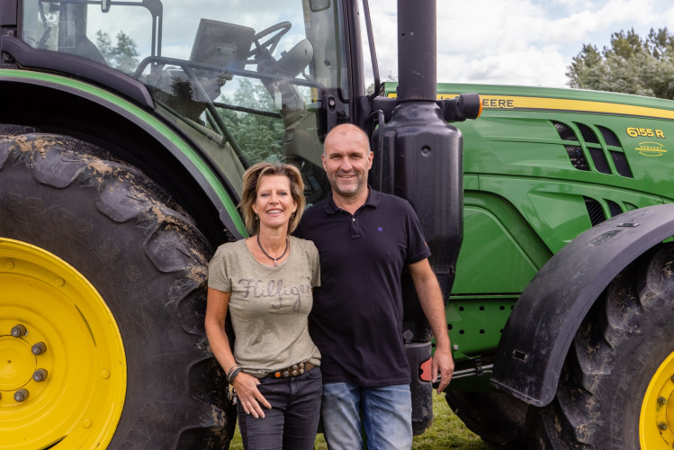 Two people standing in front of a large green John Deere tractor at FarmCamps De Kamperhoek in Zeeland, Netherlands.