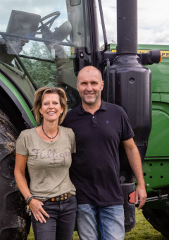 Dos personas de pie frente a un gran tractor John Deere verde en FarmCamps De Kamperhoek en Zeeland, Países Bajos.