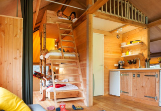 Children play in a cozy wooden cabin with bunk beds and kitchenette at FarmCamps De Kamperhoek, Zeeland.