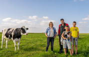 En familie står på en grøn mark med en ko og en hund hos FarmCamps De Oostermaat i Overijssel.