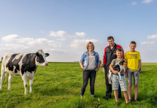 Een familie poseert in het groene veld met een koe en een hond bij FarmCamps De Oostermaat, Overijssel.