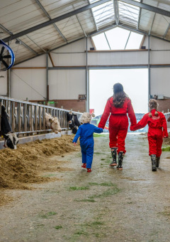 Kinderen en een volwassene lopen in kleurrijke overalls in de koeienstal van FarmCamps De Oostermaat, Overijssel.