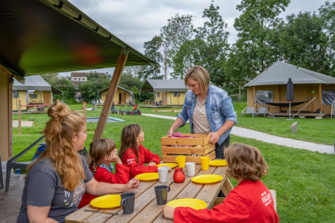 Gezin geniet van buitentafel bij FarmCamps De Oostermaat, omgeven door tenten in Overijssel, Nederland.
