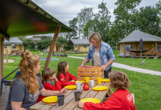 Gezin geniet van buitentafel bij FarmCamps De Oostermaat, omgeven door tenten in Overijssel, Nederland.