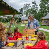 Gezin aan picknicktafel bij FarmCamps De Oostermaat, omringd door tenten in Overijssel, Nederland.