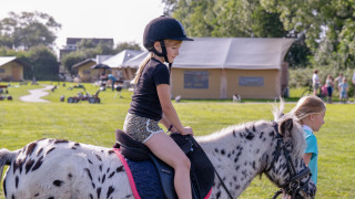 Een meisje rijdt met helm op een gevlekte pony bij FarmCamps De Oostermaat vakantiepark in Overijssel.