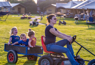 Vrouw bestuurt tractor met drie vrolijke kinderen in een kar bij FarmCamps De Oostermaat, Overijssel.