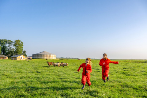 Twee kinderen in rode pakken rennen op het gras bij FarmCamps De Oostermaat in Overijssel, Nederland.