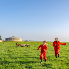 Twee kinderen in rode overalls rennen op het gras bij FarmCamps De Oostermaat in Overijssel, Nederland.