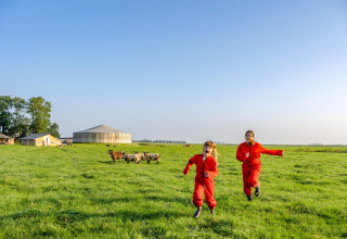 Twee kinderen in rode overalls rennen op het gras bij FarmCamps De Oostermaat in Overijssel, Nederland.