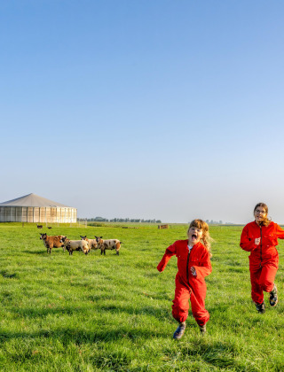 Twee kinderen in rode overalls rennen op het gras bij FarmCamps De Oostermaat in Overijssel, Nederland.