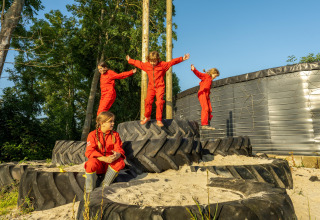 Kinderen in rode pakken spelen op grote tractorbanden bij FarmCamps De Oostermaat in Overijssel, Nederland.