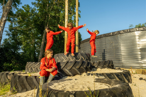 Bambini in tuta rossa giocano su grandi pneumatici da trattore a FarmCamps De Oostermaat, Overijssel, Paesi Bassi.