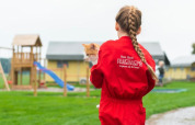 Un bambino con tuta rossa FarmCamps tiene un gatto a FarmCamps De Oostermaat, Overijssel, Paesi Bassi.