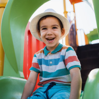 Niño sonriente con sombrero en un tobogán de parque infantil en un parque vacacional con glamping.