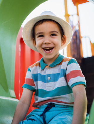 Niño sonriente con sombrero en un tobogán de parque infantil en un parque vacacional con glamping.