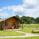 Tienda safari llamada Lodgetent en un campo verde con mesa de picnic bajo cielo azul y nubes.