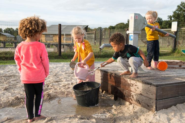 Kinderen spelen met water en zand bij een pomp op FarmCamps Alpaca Vorstenbosch in Noord-Brabant, Nederland.