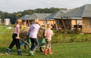 Children push a wheelbarrow filled with hay near safari tents at FarmCamps Alpaca Vorstenbosch, Netherlands.