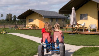 Dos niños en un kart a pedales pasan frente a tiendas en FarmCamps Alpaca Vorstenbosch en Brabante Septentrional.