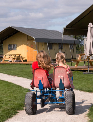 Dos niños en un kart a pedales pasan frente a tiendas en FarmCamps Alpaca Vorstenbosch en Brabante Septentrional.
