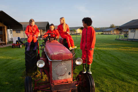 Enfants en combinaisons rouges jouant sur un vieux tracteur à FarmCamps Hoeve Sonneclaer, Drenthe, Pays-Bas.