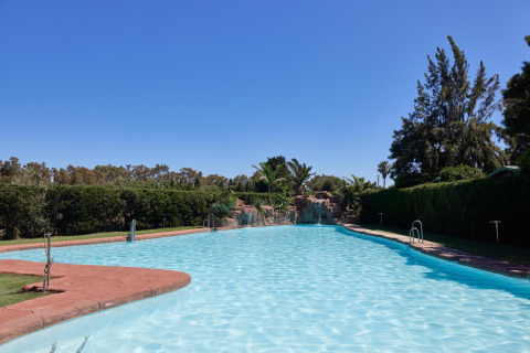 Großer Außenpool im Ferienpark TAIGA Tarifa in Andalusien, Spanien, umgeben von Garten und Palmen.