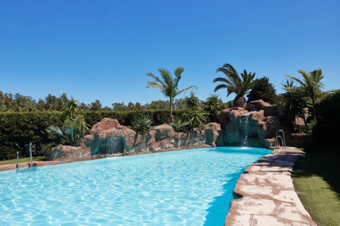 Udendørs swimmingpool med sten, palmer og vandfald på TAIGA Tarifa feriepark i Andalusien, Spanien.