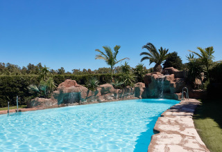 Buitenzwembad met rotsen, palmbomen en watervallen bij TAIGA Tarifa vakantiepark in Andalusië, Spanje.