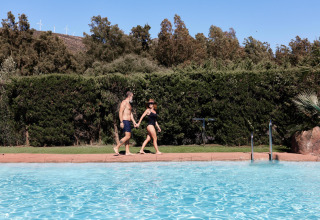 Zwei Personen im Badeanzug gehen Hand in Hand am Poolrand im TAIGA Tarifa Ferienpark, Andalusien, Spanien.