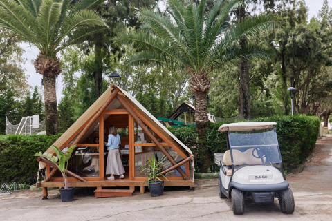 Kleine Glampinghütte und Golfwagen unter Palmen im Ferienpark TAIGA Tarifa in Andalusien, Spanien.