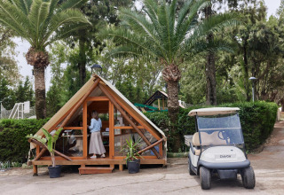 Pequeña cabaña glamping y carrito de golf bajo palmeras en el parque vacacional TAIGA Tarifa, Andalucía.