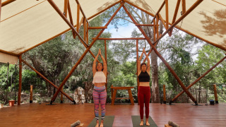 Dos mujeres practicando yoga bajo una carpa abierta en el parque vacacional TAIGA Tarifa en Andalucía, España.