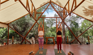 Dos mujeres practicando yoga bajo una carpa abierta en el parque vacacional TAIGA Tarifa en Andalucía, España.