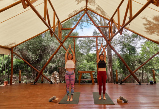 Deux femmes pratiquant le yoga sous une tente ouverte au parc de vacances TAIGA Tarifa en Andalousie, Espagne.
