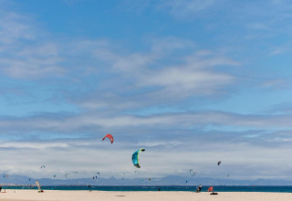 Strand und Kitesurfer bei TAIGA Tarifa, Andalusien, Spanien, unter blauem Himmel mit Wolken.